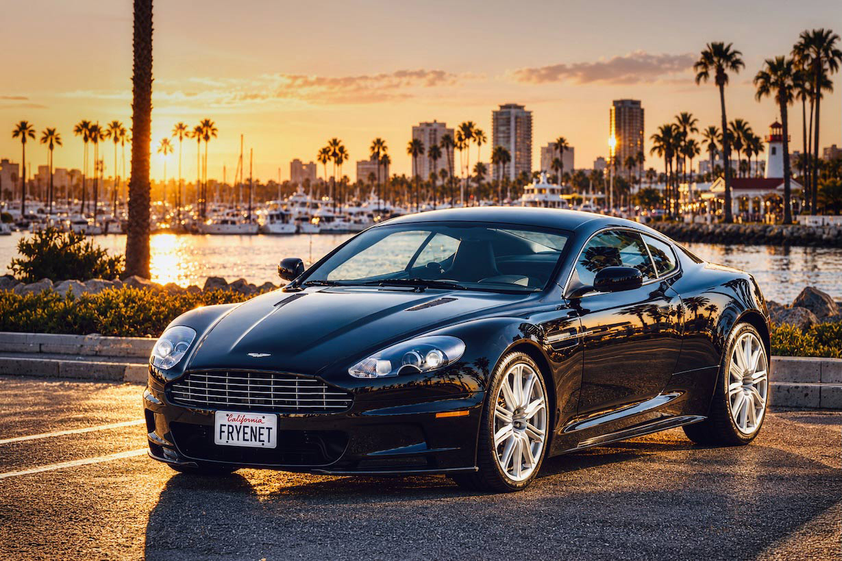 Vintage-style photograph of a sports car beside a waterfront with palm trees and a city skyline.